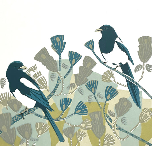 a pair of magpies are shown sitting among pine tree branches in a modern style.  The foliage of the tree is shown using bold geometric shapes using airforce blue, olive green, duck egg blue, beige, and pale sand colours.  The design is simple and striking and the inky coloured magpies stand out against the white of the paper.  
